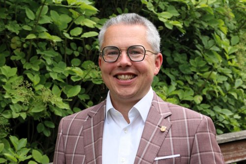 Dr. Tepe steht vor einer Hecke und lächelt in die Kamera.