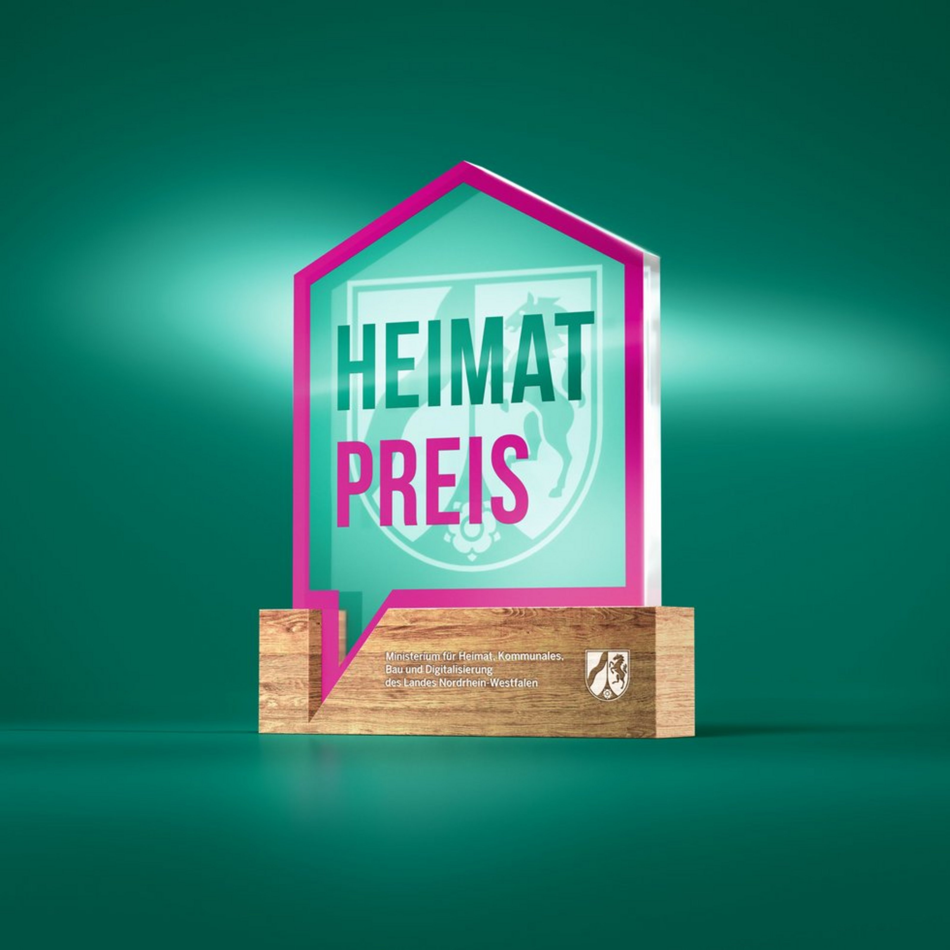 Man sieht eine kleine Skulptur aus Glas auf einem Holzsockel. Das Glas ist wie ein Haus geformt und trägt die Beschriftung Heimatpreis.
