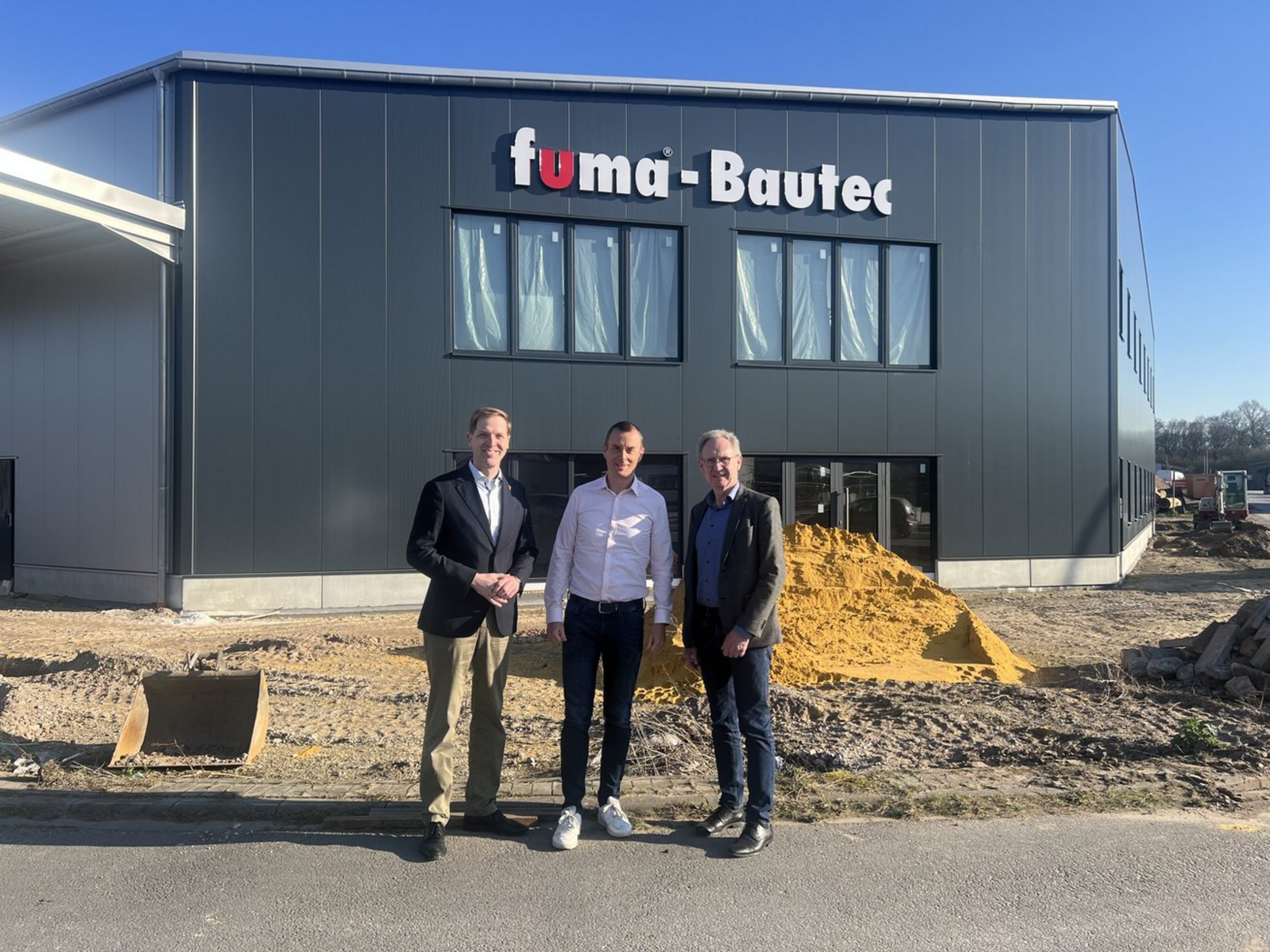 Drei Männer stehen vor dem Firmengebäude von Fuma Bautec und sprechen über die Entwicklung des Unternehmens.
