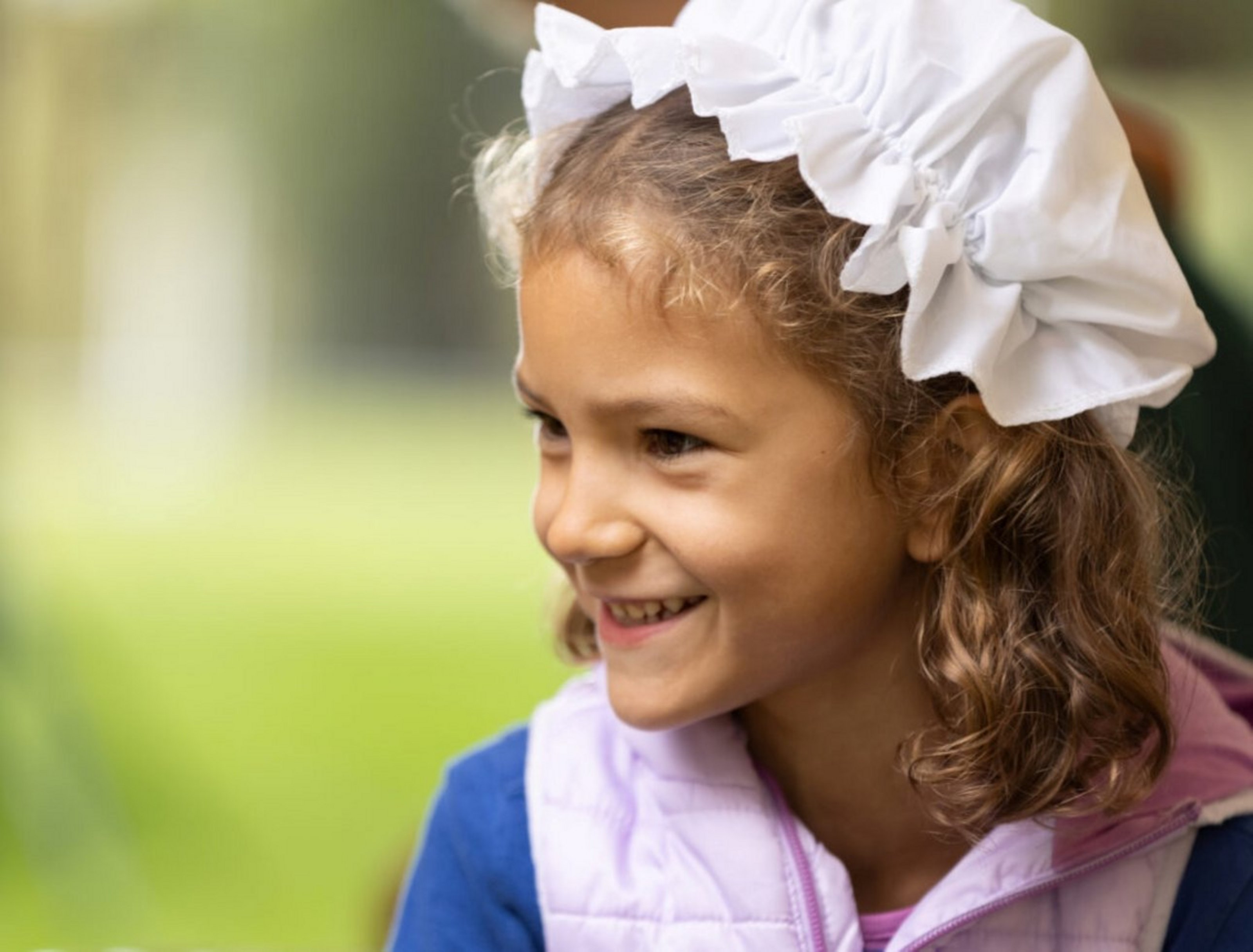 Ein Mädchen trägt eine weiße Haube und lächelt. Der Hintergrund ist grün.