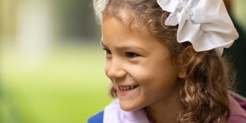 Ein Mädchen trägt eine weiße Haube und lächelt. Der Hintergrund ist grün.