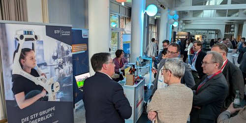 Sieben Männer in Anzug stehen vor einem Messestand.