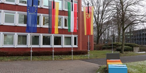 An einem roten Gebäude sind die Kreis-, Landes-, Bundes- und Europaflagge mit Trauerflor gehisst.