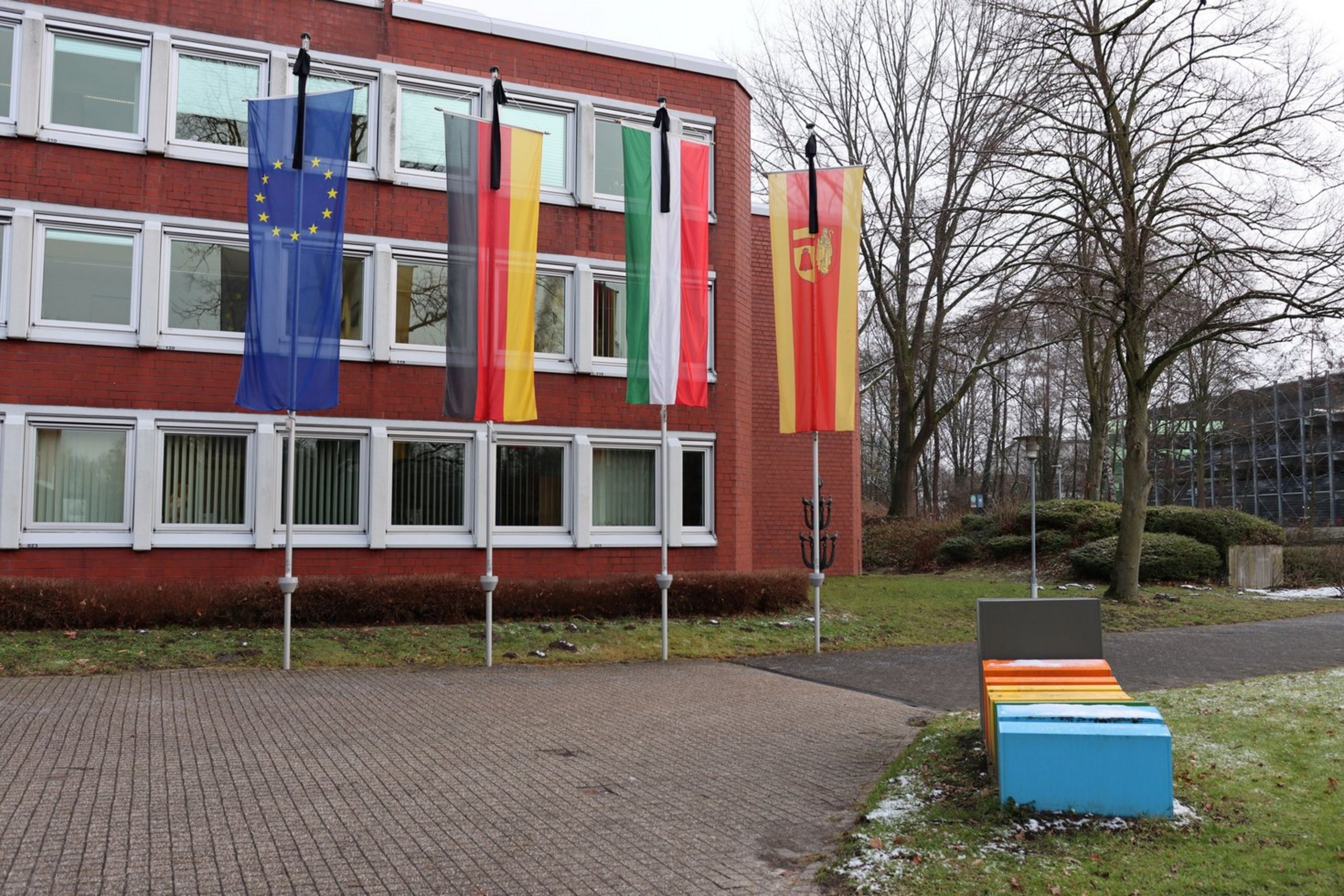 An einem roten Gebäude sind die Kreis-, Landes-, Bundes- und Europaflagge mit Trauerflor gehisst.