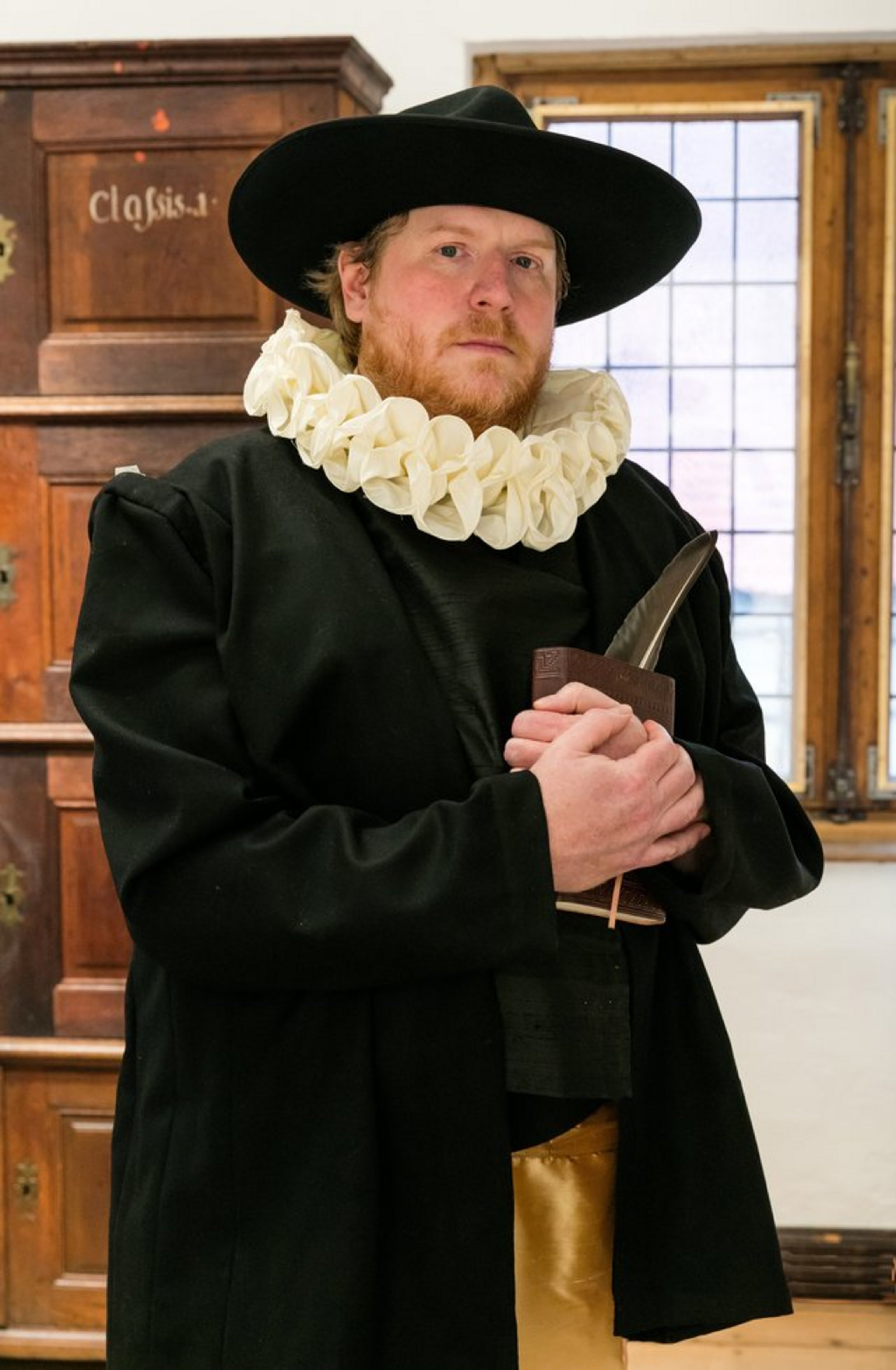 Ein Mann in altertümlicher Kleidung steht in einem Burgsaal.