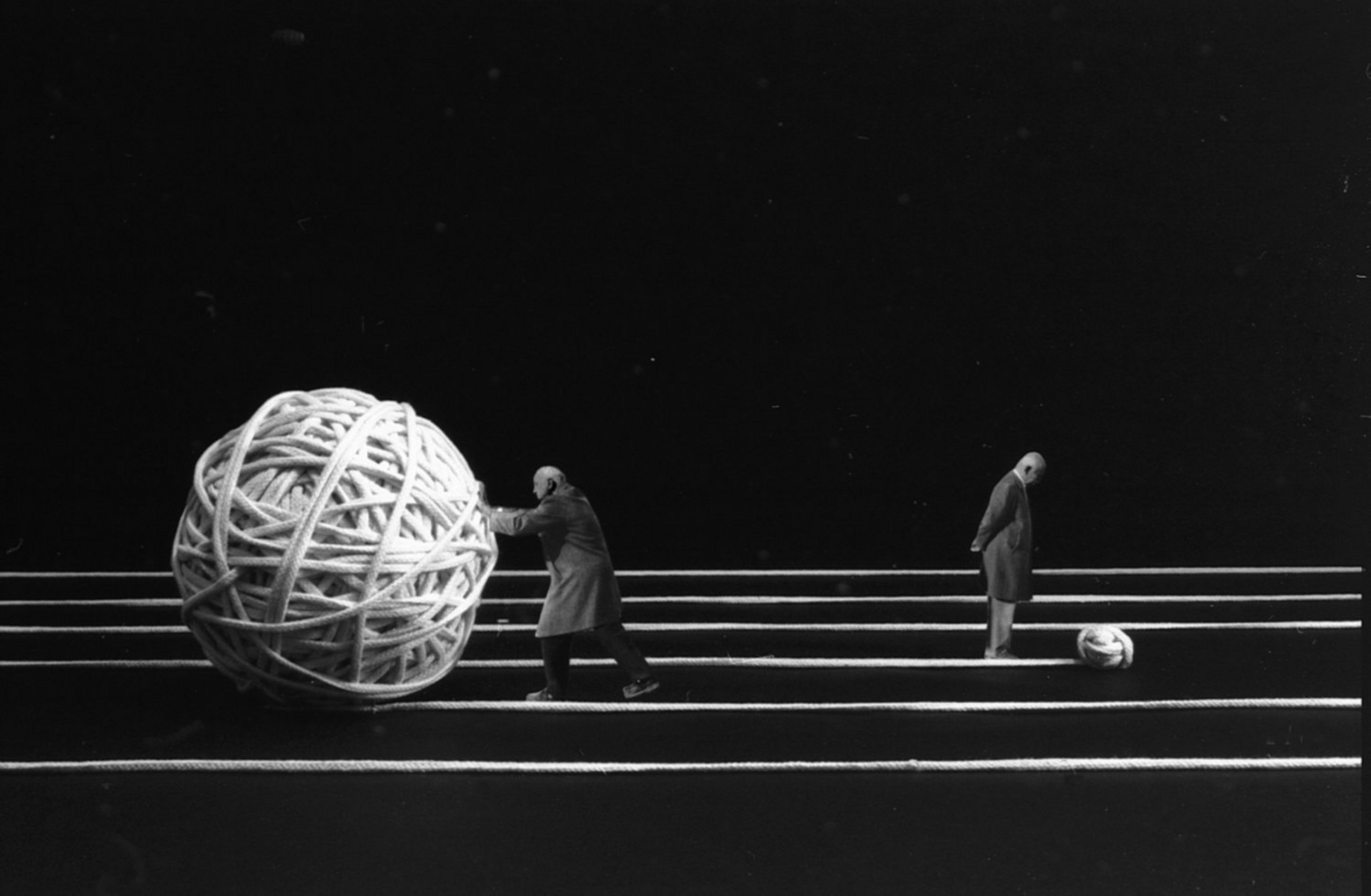 Man sieht ein künsterlisches Foto von einem Mann, der ein überdimensionalen Wollball vor sich her schiebt.