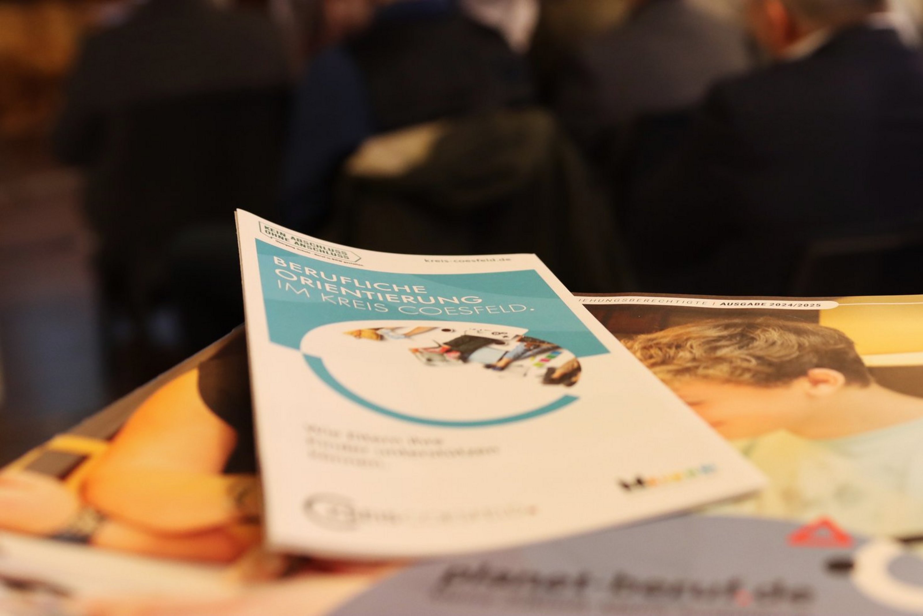 Ein Flyer liegt auf einem Tisch. Das Design ist in blau und weiß gehalten und trägt die Aufschrift "Berufliche Orientierung im Kreis Coesfeld".