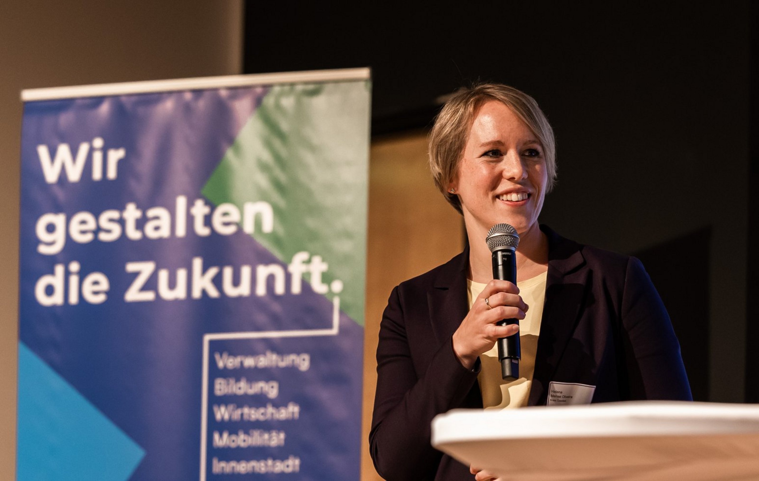 Frau mit Mikrofon vor Banner mit Text 'Wir gestalten die Zukunft'