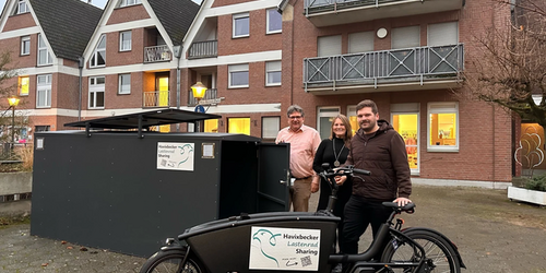 Drei Personen stehen hinter einem schwarzen Lastenfahrrad mit Aufkleber "Havixbecker Lastenrad Sharing" vor einem Wohnhaus mit Giebel und Balkonen