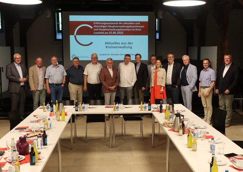 Gruppenfoto aktueller und ehemaliger Hauptverwaltungsbeamter beim Austausch auf Burg Vischering vor einer Präsentationsfolie zur Kreisverwaltung.