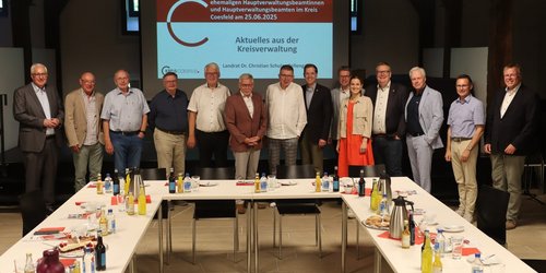 Gruppenfoto aktueller und ehemaliger Hauptverwaltungsbeamter beim Austausch auf Burg Vischering vor einer Präsentationsfolie zur Kreisverwaltung.