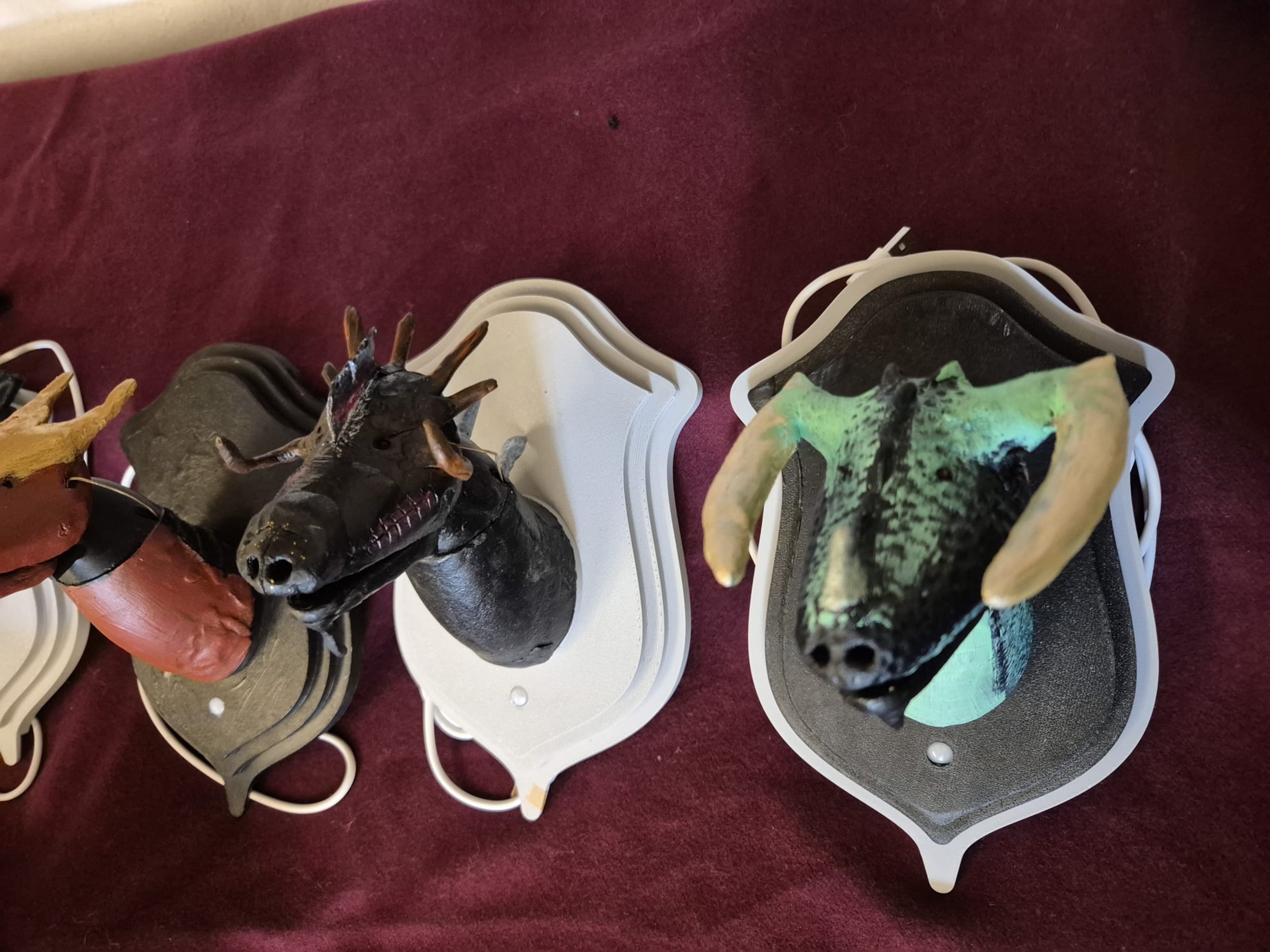 Man sieht selbstgebastelte Drachenköpfe, die wie Trophäen auf Holzplatten angebracht sind.