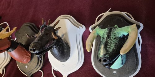 Man sieht selbstgebastelte Drachenköpfe, die wie Trophäen auf Holzplatten angebracht sind.