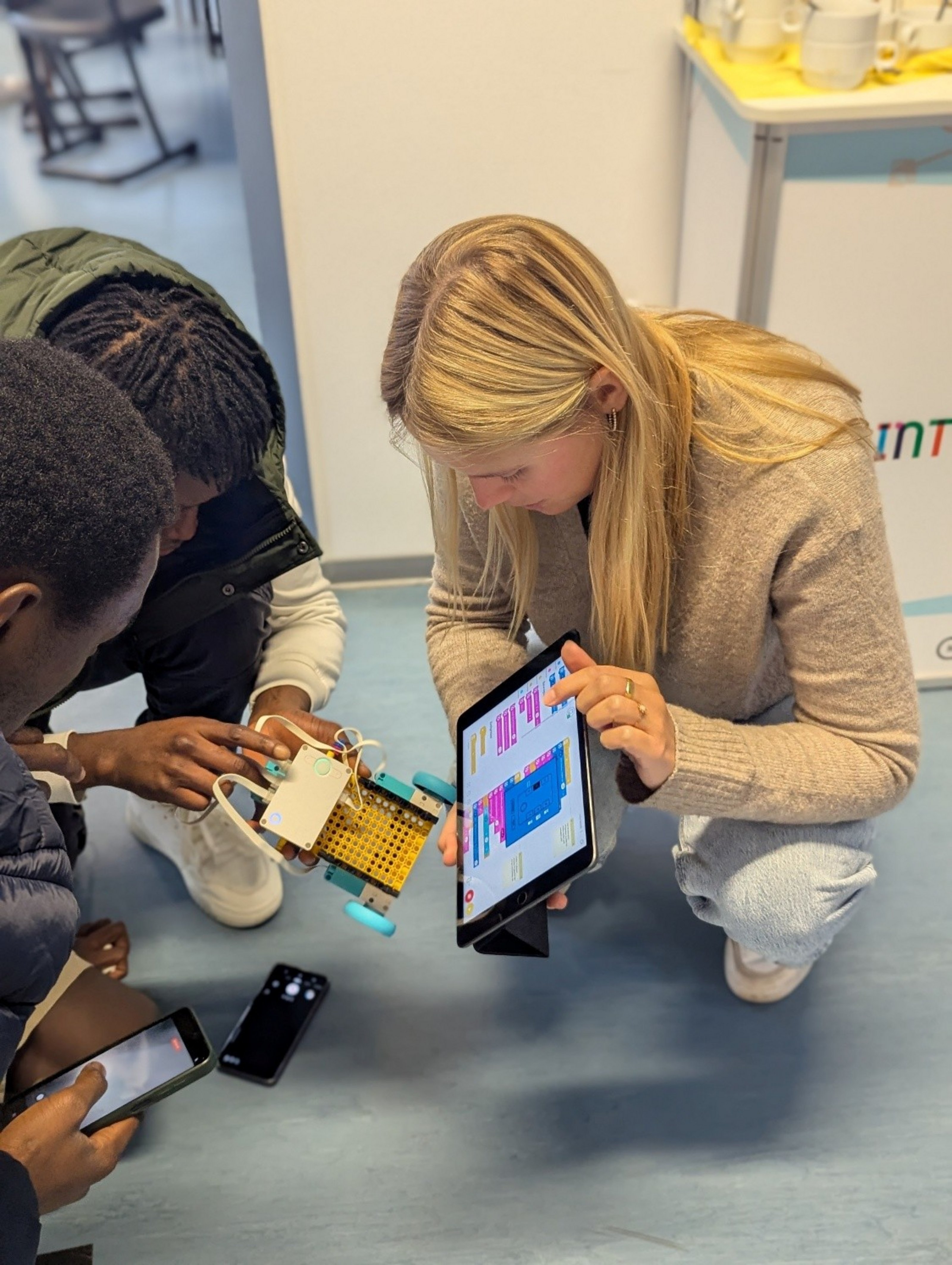 Eine Frau und zwei Jugendliche programmieren gemeinsam einen kleinen Roboter mithilfe eines Tablets.