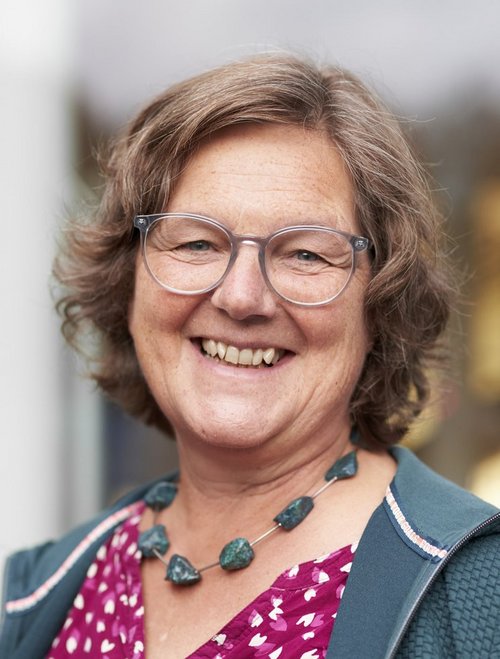 Eine Frau mit Brille und pink-gepunktetem Oberteil blickt lachend in die Kamera.