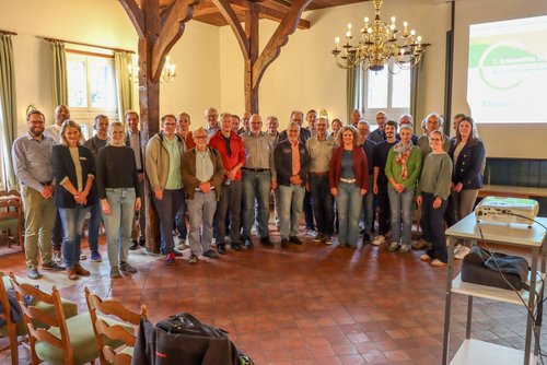 Eine Gruppe von Personen steht im Halbkreis in einem hellen Raum und blickt in die Kamera.