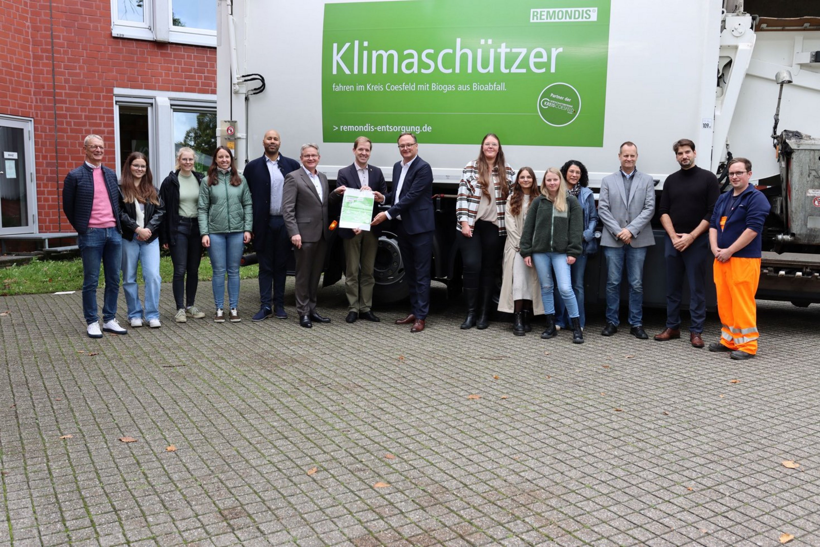 Unter dem Motto „Saubere Antriebe für Sammelfahrzeuge“ informierten der Kreis Coesfeld, die Wirtschaftsbetriebe Kreis Coesfeld GmbH (WBC) und das Entsorgungsunternehmen Remondis über den Einsatz von Biogas-Fahrzeugen in der kommunalen Abfallsammlung Eine Gruppe von 15 Personen steht vor einem weißen Müll-Fahrzeug, auf dem ein grüner Aufdruck mit der Aufschrift "Klimaschützer" befestigt ist.