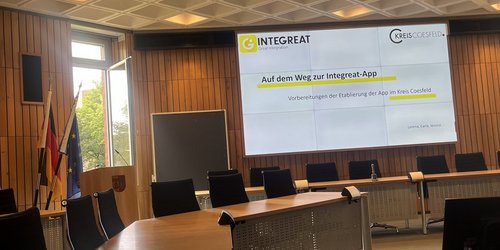 Auf einer Bildschirmpräsentation in einem Sitzungssaal steht "Auf dem Weg zur Integrat-App. Vorbereitung der Etablierung der App im Kreis Coesfeld".