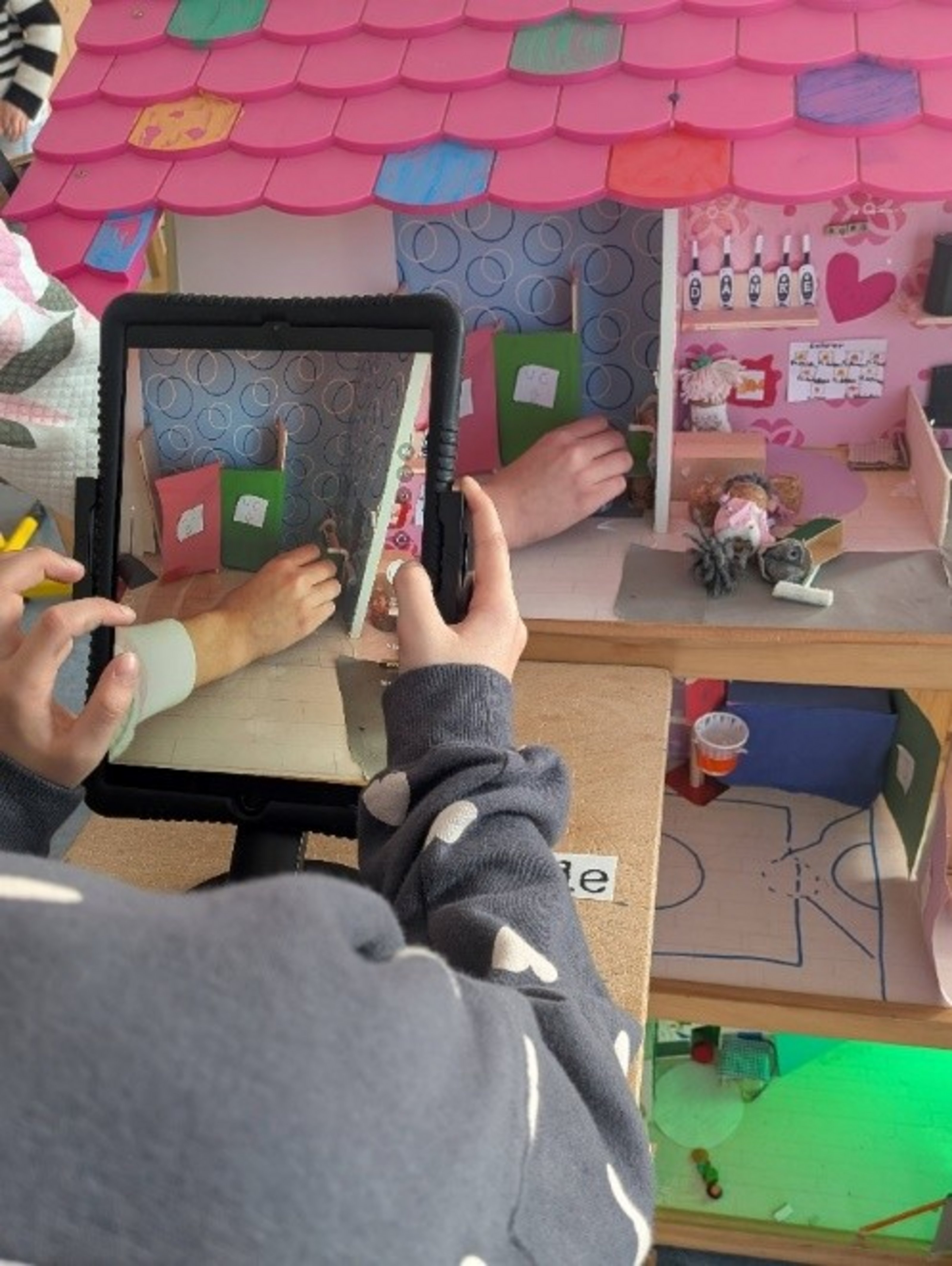 Es ist ein Bildschirm eines Tablets zu sehen, das eine Szene in einem Puppenhaus filmt.