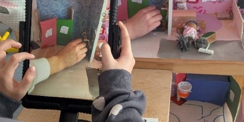 Es ist ein Bildschirm eines Tablets zu sehen, das eine Szene in einem Puppenhaus filmt.