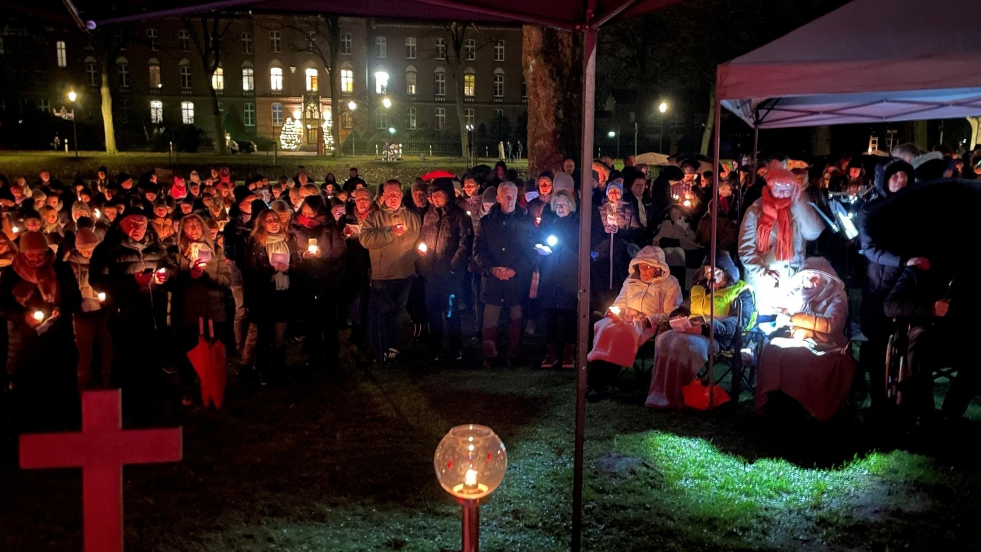 Eine Menschenmenge steht draußen im Dunkeln auf einer Wiese und hält einen Gottesdienst.