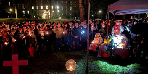 Eine Menschenmenge steht draußen im Dunkeln auf einer Wiese und hält einen Gottesdienst.