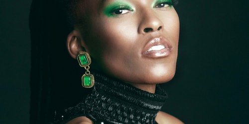 Das Foto ist eine Porträtaufnahme einer Frau mit grünem Lidschatten, grünen Ohrringen und schwarzem Oberteil.