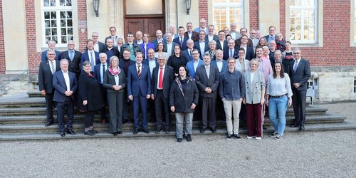 Eine Gruppe von ca.. 60 Personen steht auf den Treppenstufen vor einem alten Backsteingebäude in mehreren reihen hintereinander aufgereiht und schaut in die Kamera.