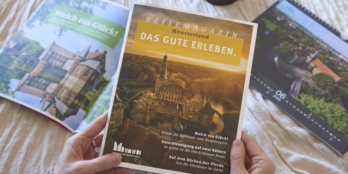 Person hält ein Reisemagazin über das Münsterland, daneben liegen weitere Hefte.
