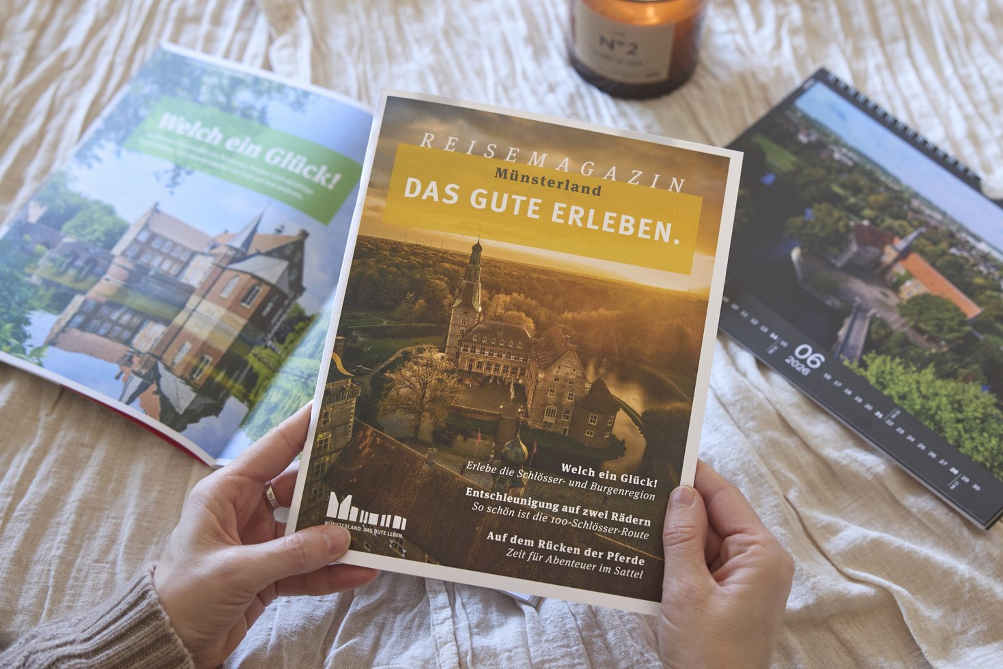 Person hält ein Reisemagazin über das Münsterland, daneben liegen weitere Hefte.