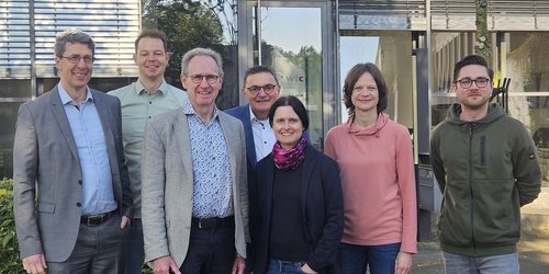 Sieben Personen stehen nebeneinander vor einer Glastür mit der Aufschrift wfc.