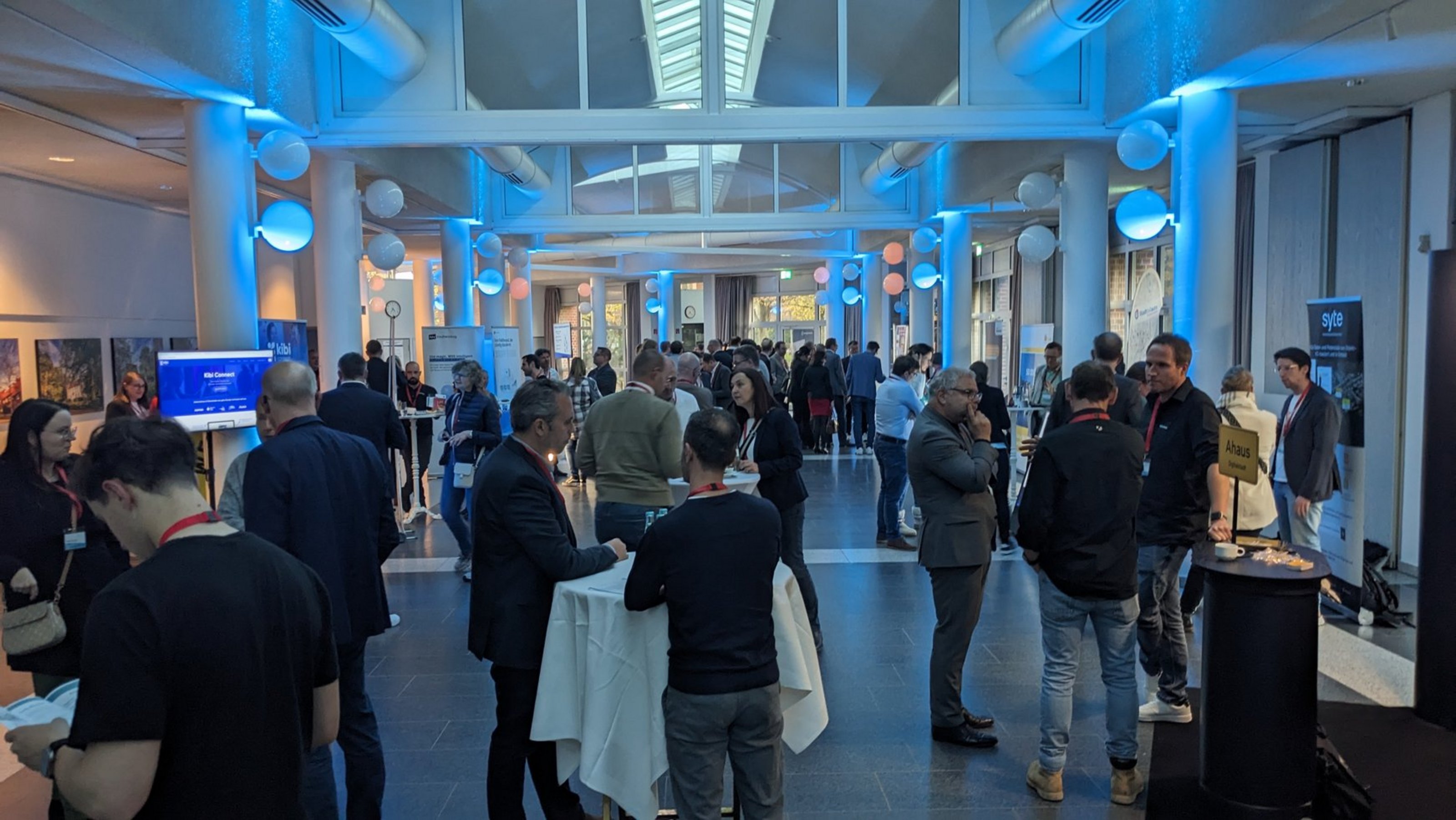 Menschen in einem hellen, modernen Konferenzraum mit Stehtischen und blauer Beleuchtung bei einer Digitalisierungskonferenz