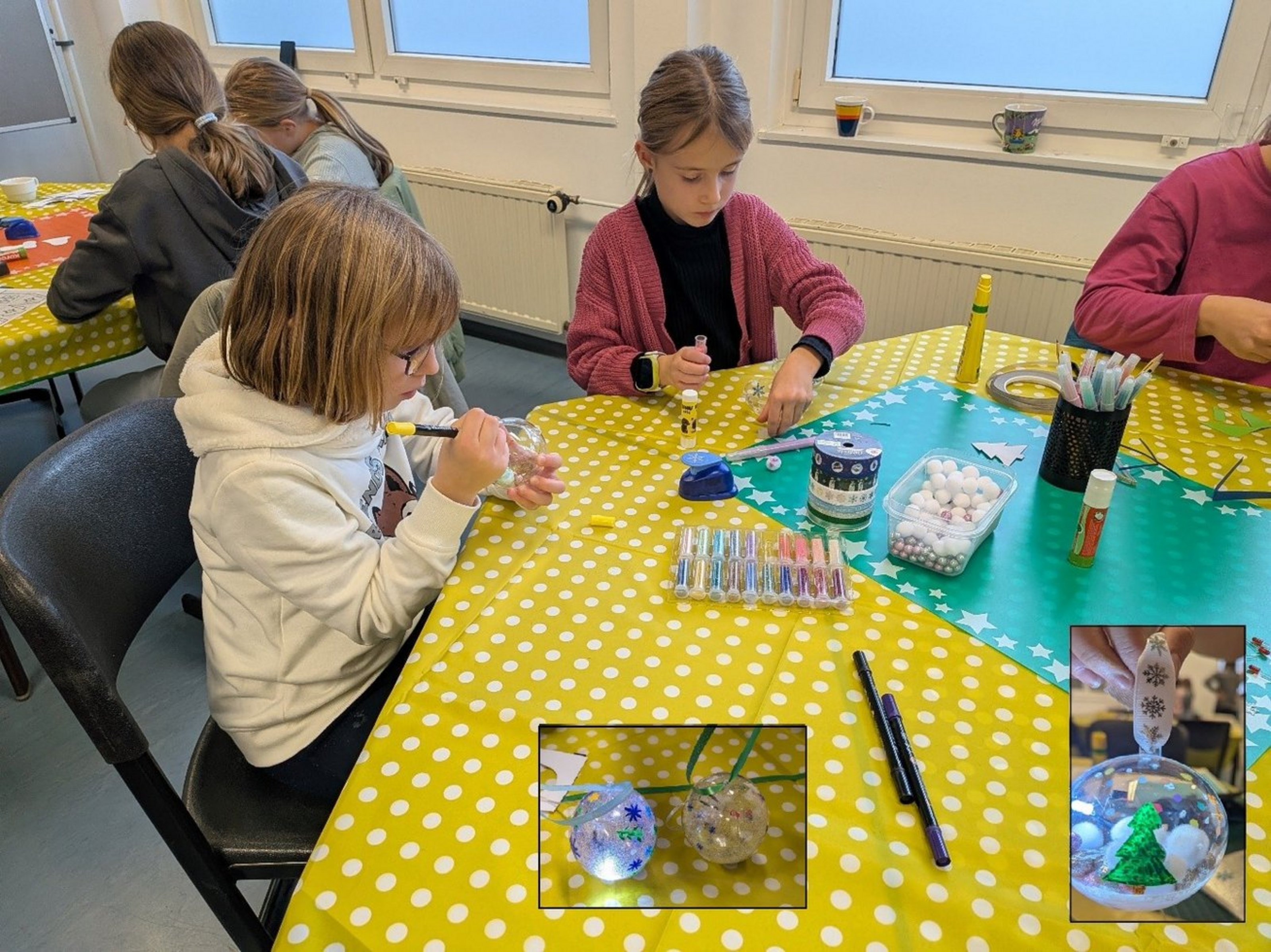 Zwei Mädchen sitzen an einem Basteltisch und gestalten mit Stiften und Materialien eine leuchtende Weihnachtskugel.