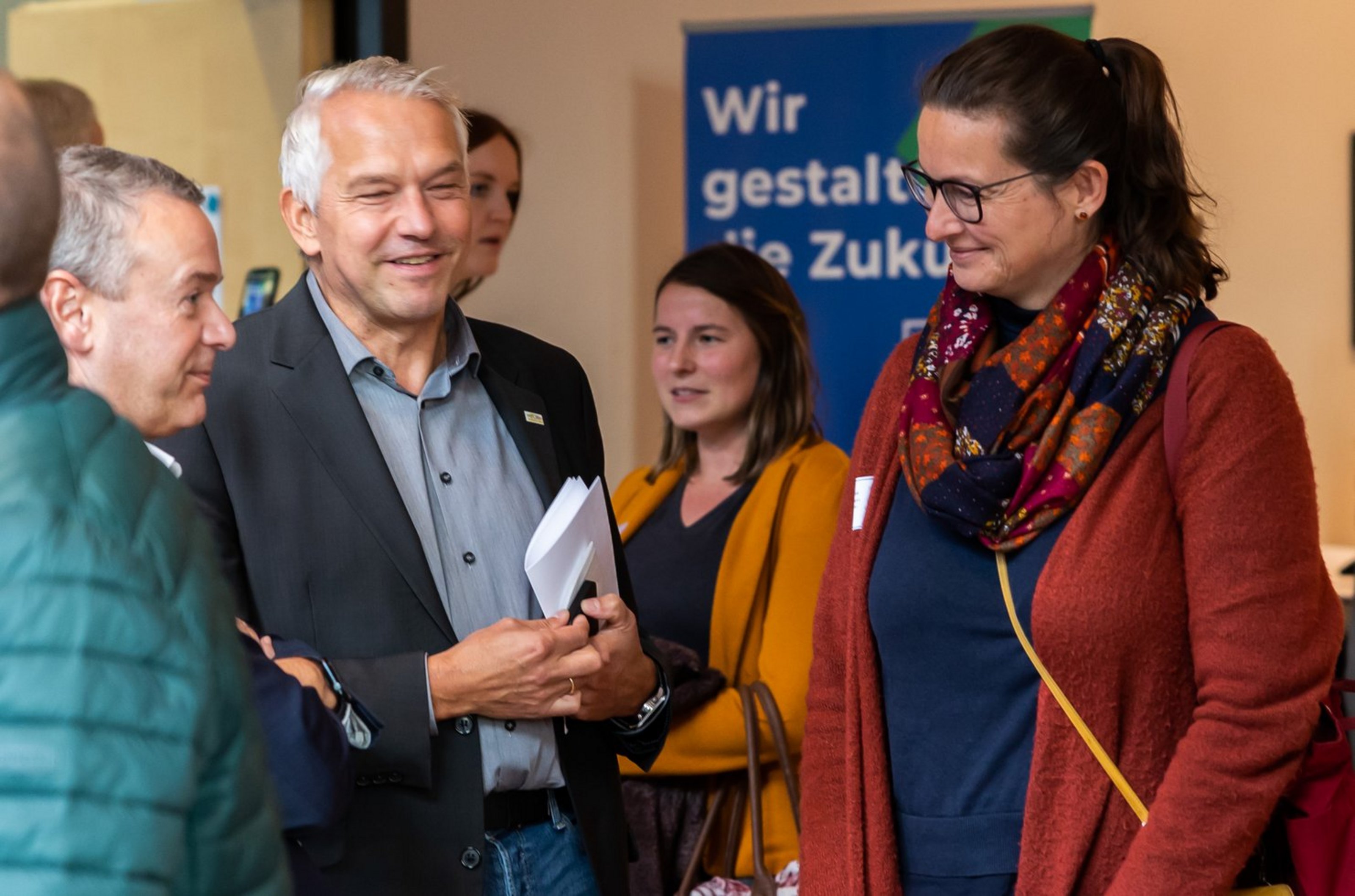 Gruppe von vier Personen im Gespräch vor einem blauen Schild mit weißer Aufschrift