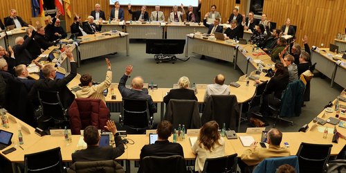 Mitglieder des Kreistags sitzen im Sitzungssaal an runden Tischen und stimmen per Handzeichen über den Kreishaushalt 2026 ab.