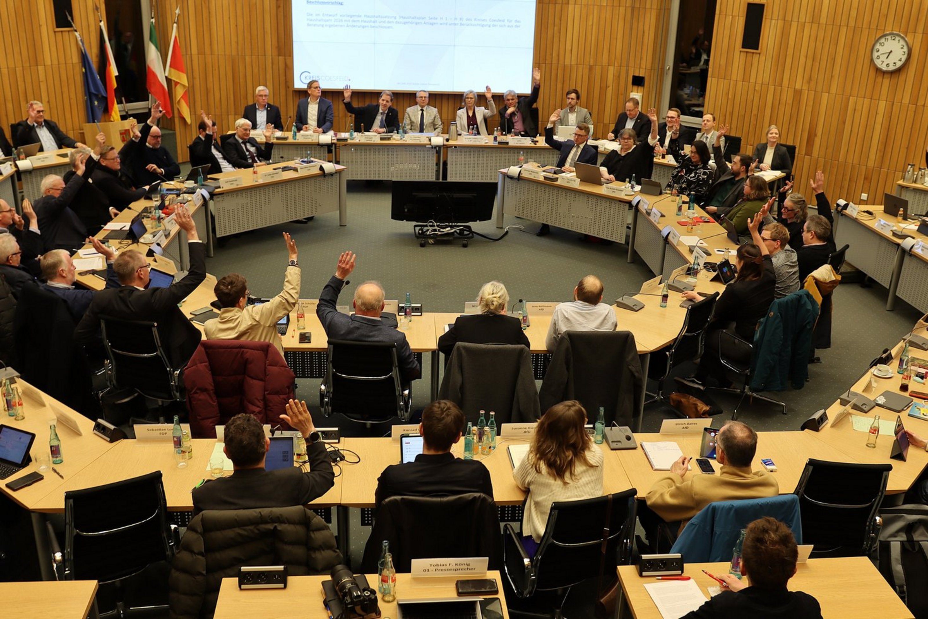 Mitglieder des Kreistags sitzen im Sitzungssaal an runden Tischen und stimmen per Handzeichen über den Kreishaushalt 2026 ab.