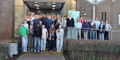 Eine Gruppe aus Jugendlichen und Erwachsenen steht auf der Treppe und einer Rampe vor einem Haus.