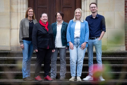 Fünf Personen stehen auf Steinstufen vor einer Eingangstür.