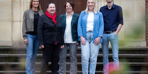 Fünf Personen stehen auf Steinstufen vor einer Eingangstür.