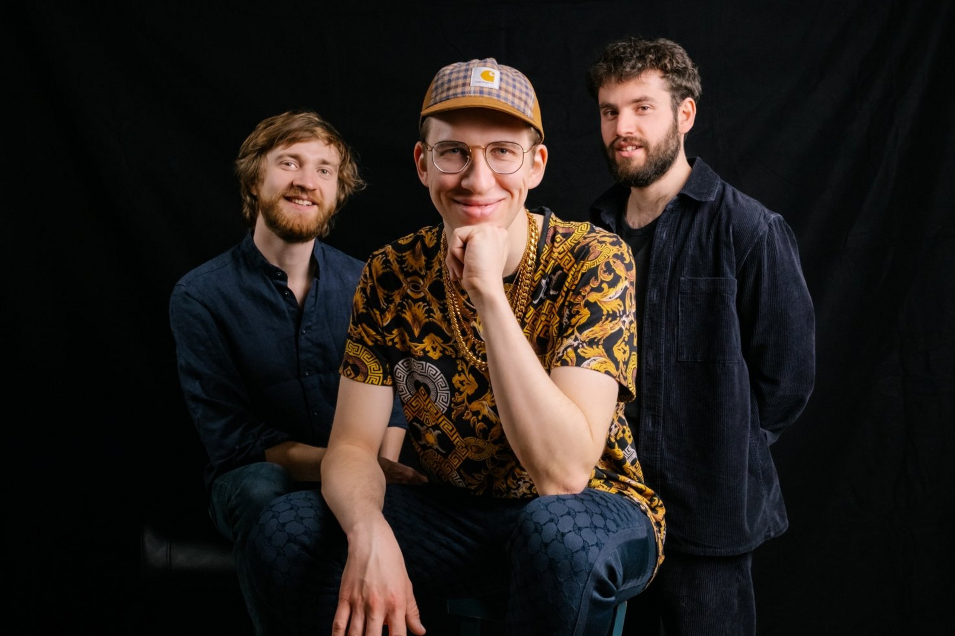 Das Nils Kugelmann Trio (Foto: Uli Neumann-Cosel) Drei Männer sind vor schwarzem Hintergrund zu sehen. Einer von ihnen kniet vorne, die anderen stehen rechts und links hinter ihm.