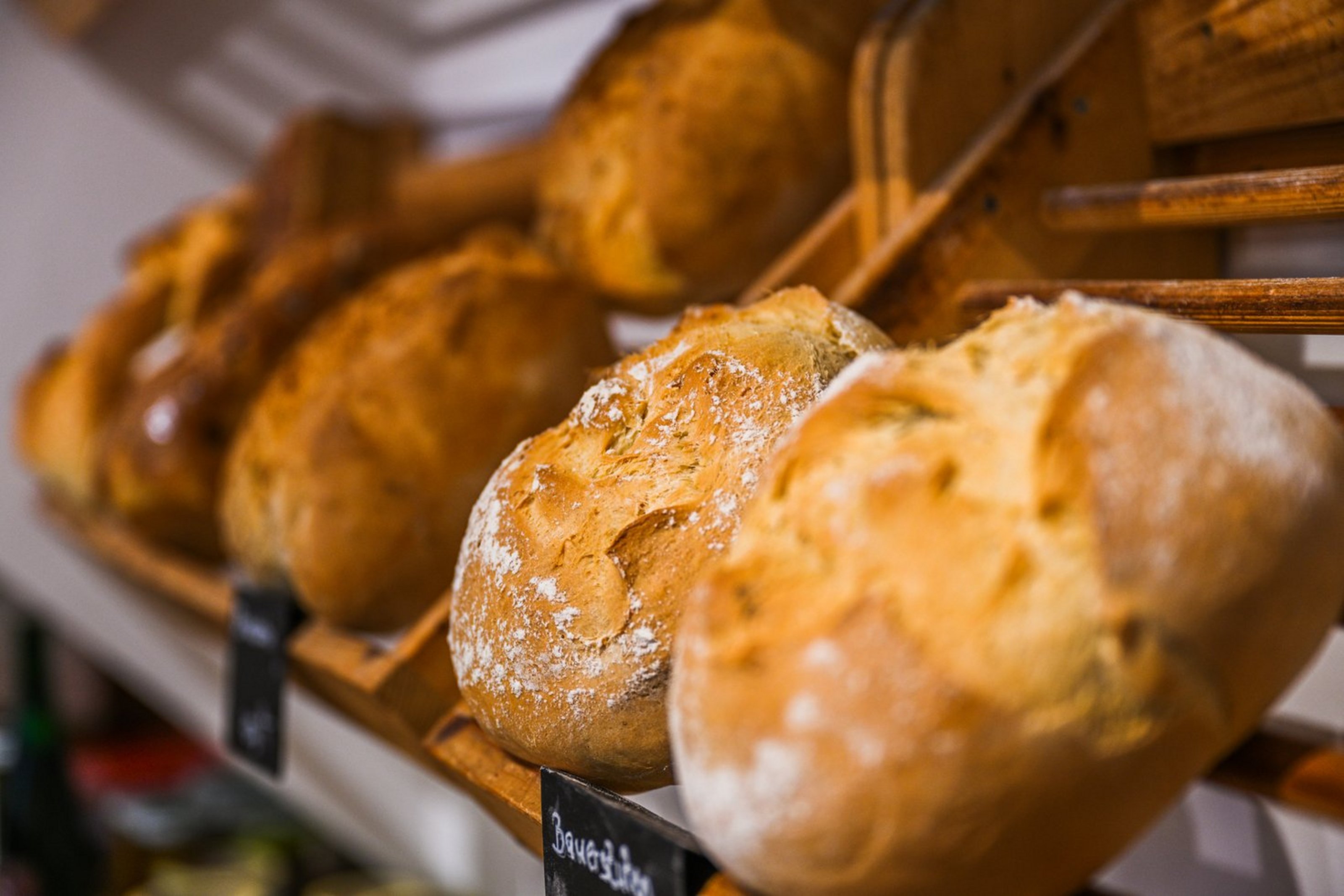 Brötchen liegen in einem schrägen Regal. Zwei kleine Schilder befinden sich an der Kante des Regals.