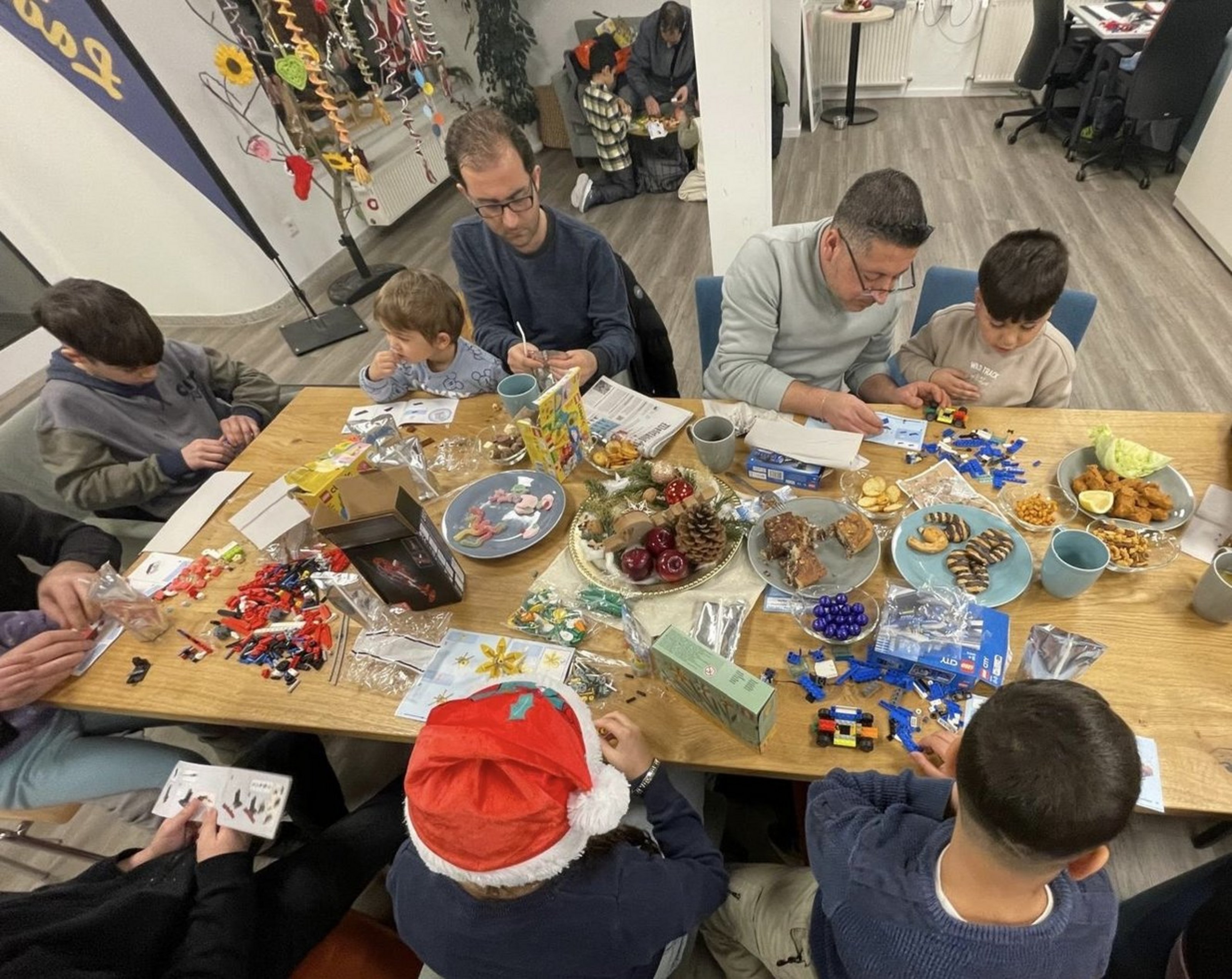 Väter und Kinder sitzen gemeinsam an einem Tisch, bauen und spielen in entspannter Atmosphäre.