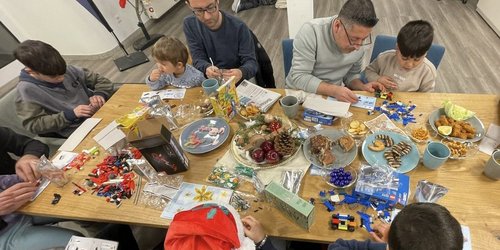 Väter und Kinder sitzen gemeinsam an einem Tisch, bauen und spielen in entspannter Atmosphäre.