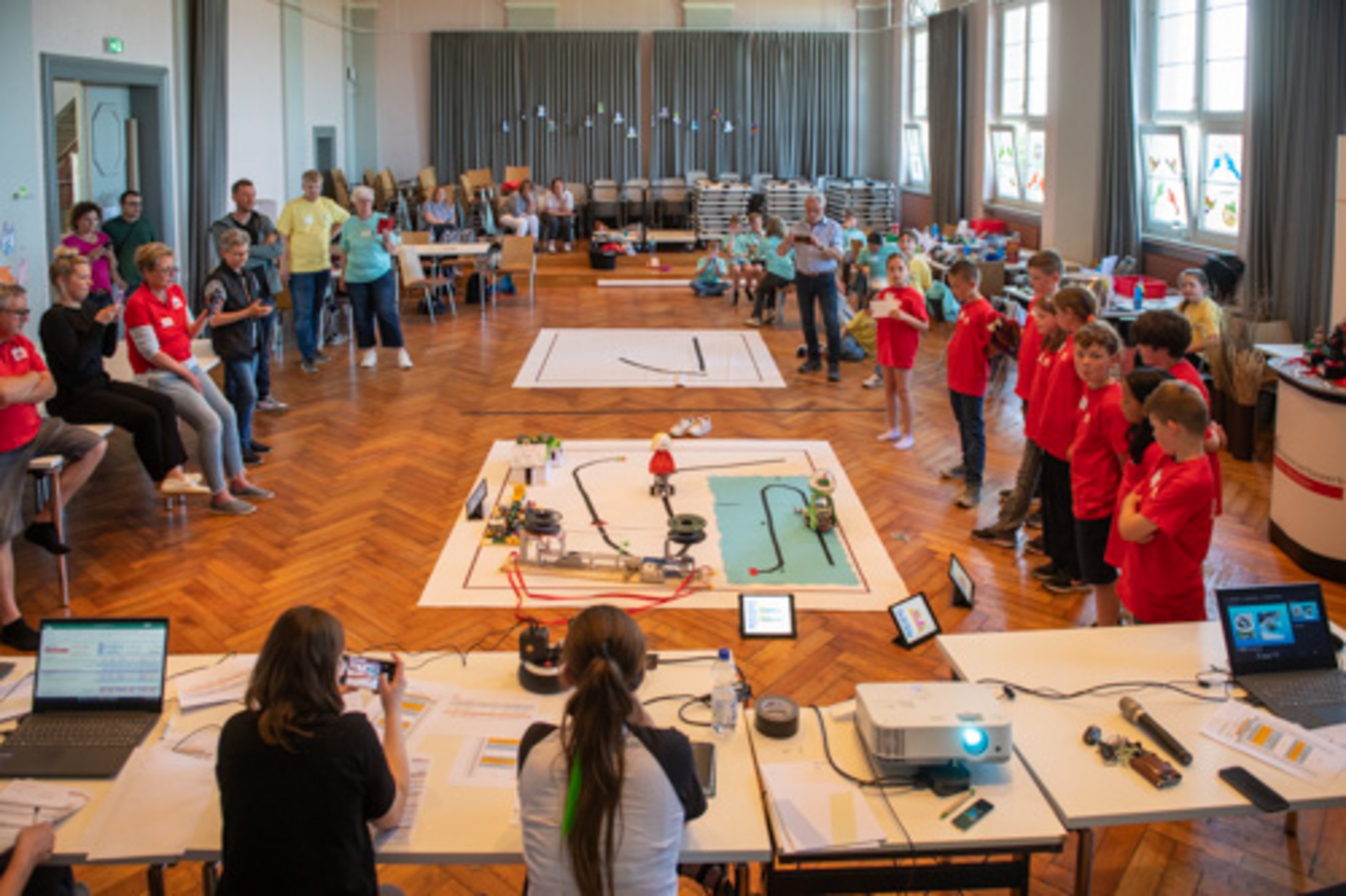 Viele Kinder und Jugendliche versammeln sich um Tische mit Robotern beim zdi-Roboterwettbewerb.