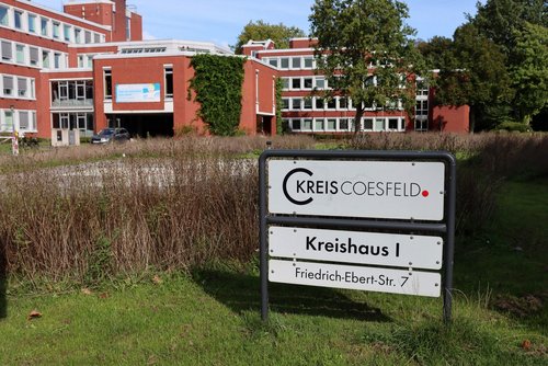 Ein weißes Schild mit der Aufschrift "Kreis Coesfeld. Kreishaus I" steht auf einer Wiese.