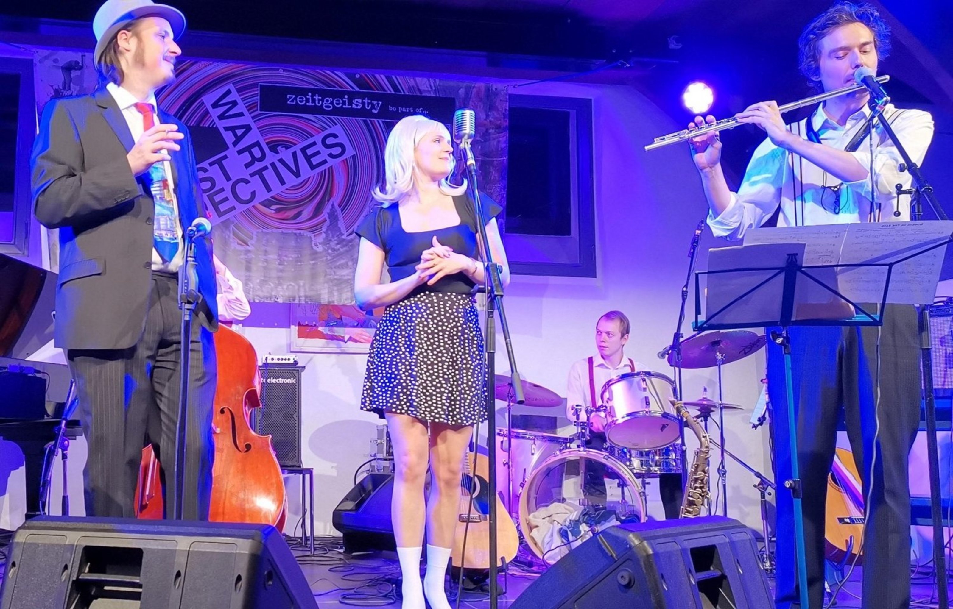 Vier Personen stehen auf einer Bühne und musizieren gemeinsam. 