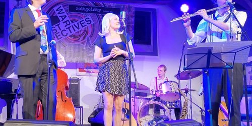 Vier Personen stehen auf einer Bühne und musizieren gemeinsam. 