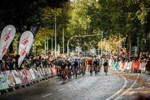 Radrennfahrerinnen und Radrennfahrer fahren beim Münsterland Giro vor jubelndem Publikum durchs Ziel.