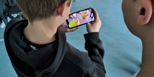 Zwei Jungen schauen auf einen Handydisplay, der zwei bunte Figuren zeigt.