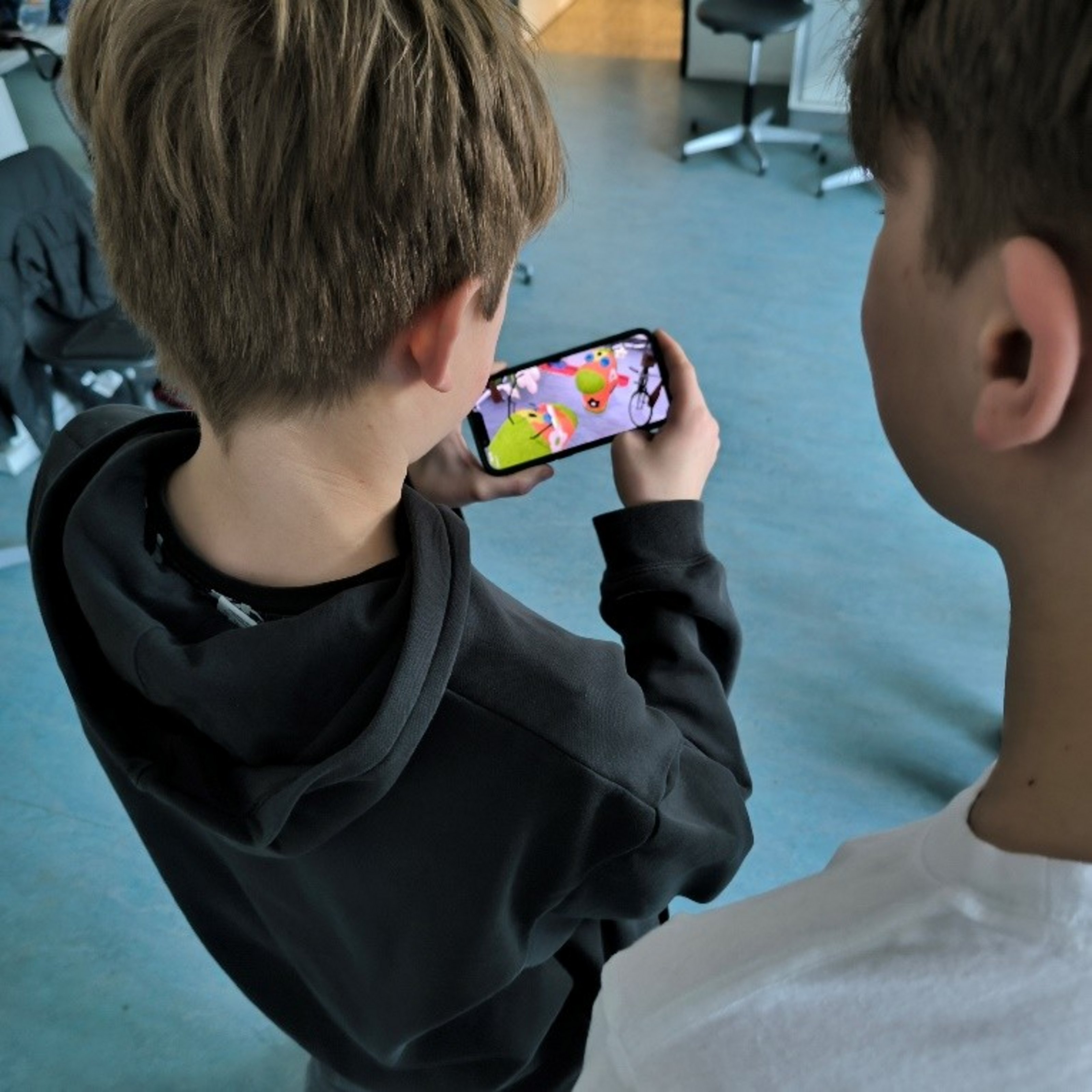 Zwei Jungen schauen auf einen Handydisplay, der zwei bunte Figuren zeigt.